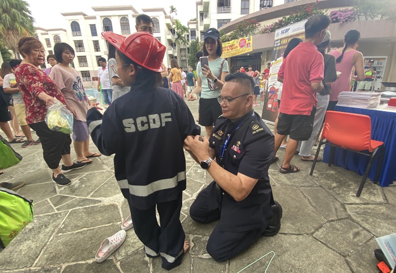 WO1 Razali helping a child wear a firefighter costume. PHOTO - SCDF : Thomas Lim